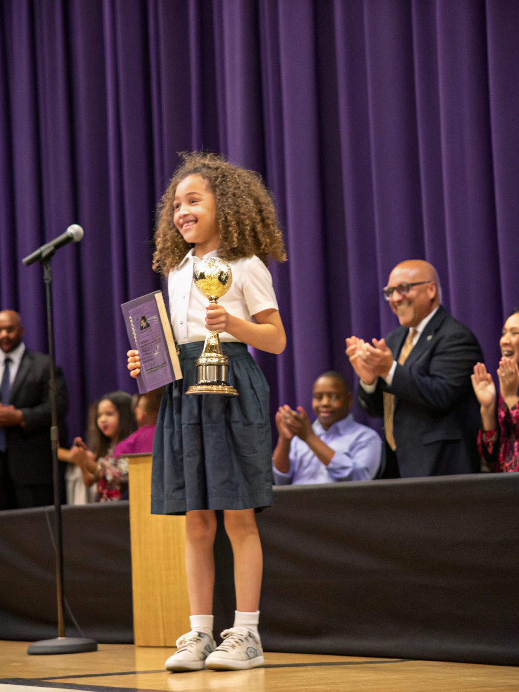 Student proudly receiving national drawing competition trophy at school morning assembly